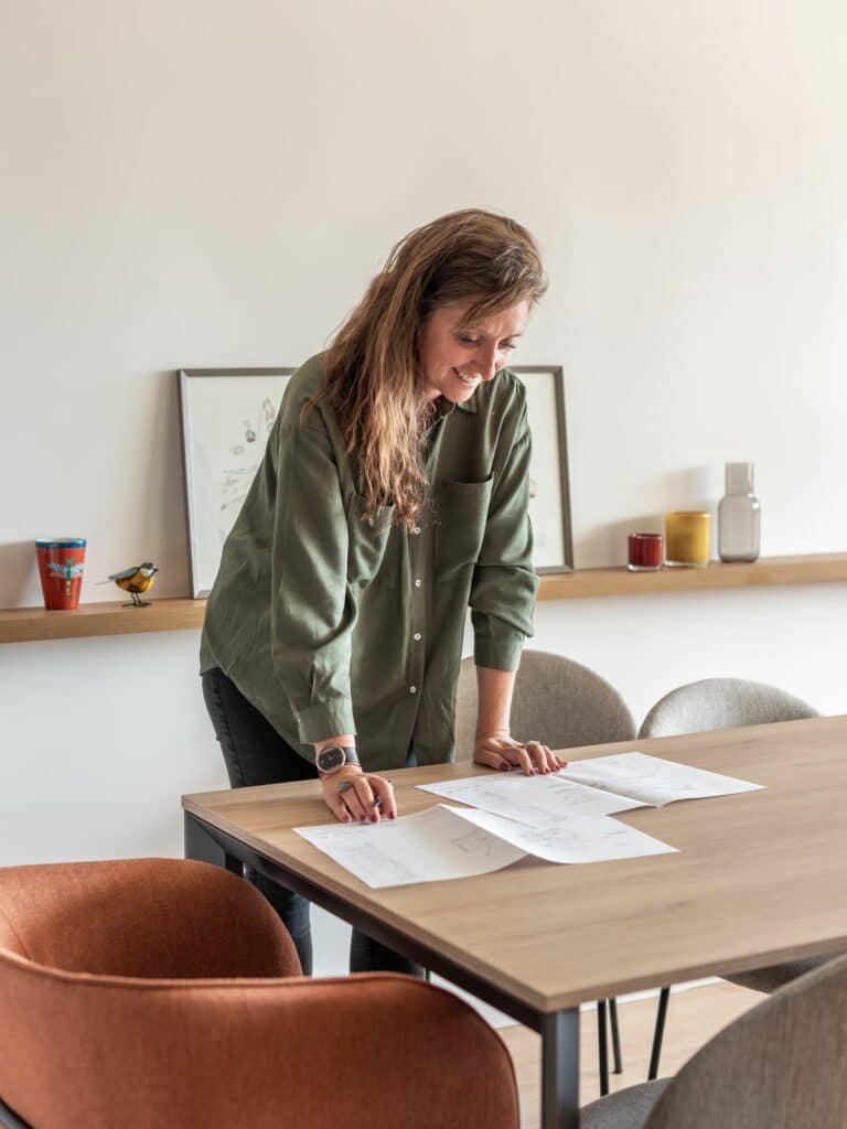 Décoratrice d'intérieur analysant les plans d'un appartement pour accompagner un client dans sa recherche de bien immobilier en Isère et dans les Alpes.